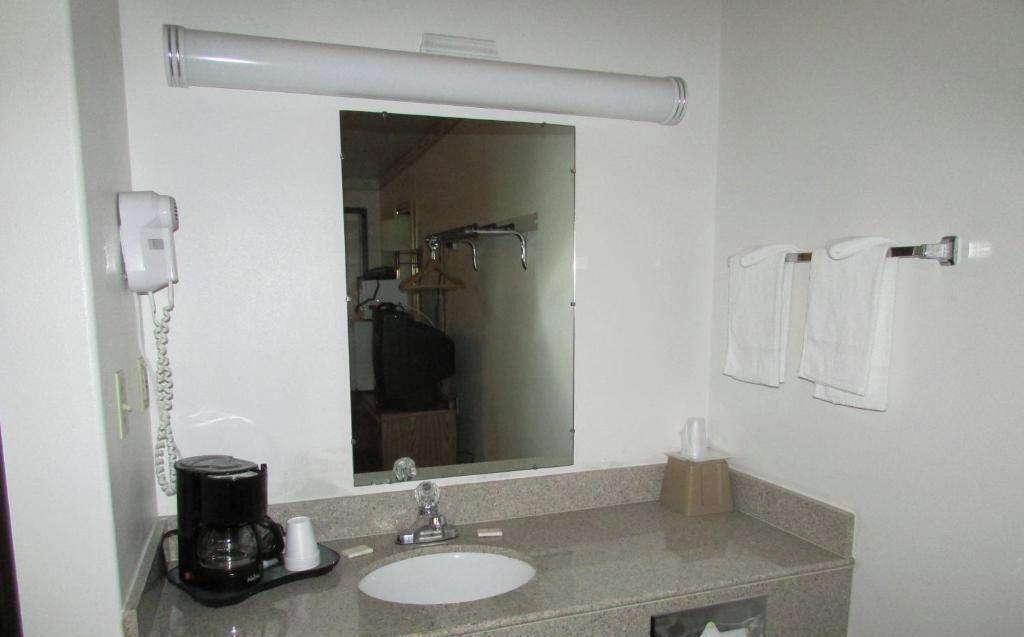 Un baño de hotel con lavamanos, espejo, toallero y secador de pelo.