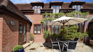 A patio with a table and chairs, a potted plant, and a brick wall. - Garden Flat -  comfortable cottage for two close to Chichester and Goodwood (Tangmere)