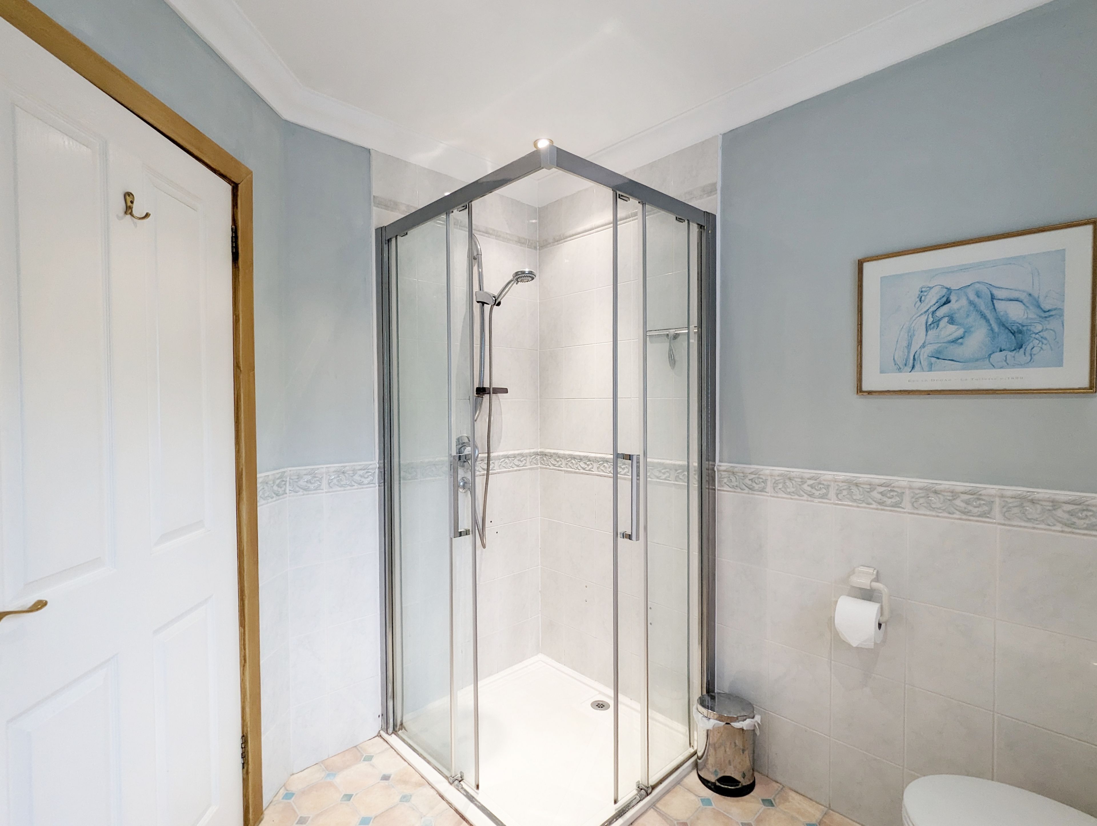 A bathroom with a glass-enclosed shower, a toilet, and a framed artwork on the wall.