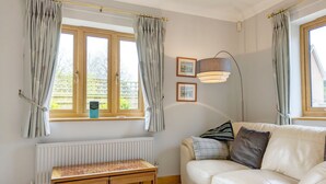 A living room with a white leather sofa, a wooden table, a floor lamp, and a window with curtains. - Garden Flat -  comfortable cottage for two close to Chichester and Goodwood (Tangmere)