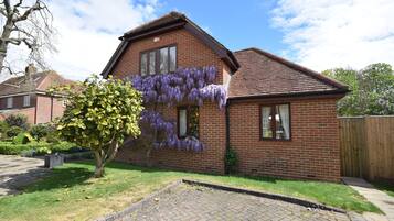 A brick house with purple flowering vines on the side, a paved driveway, and a wooden fence in the background.