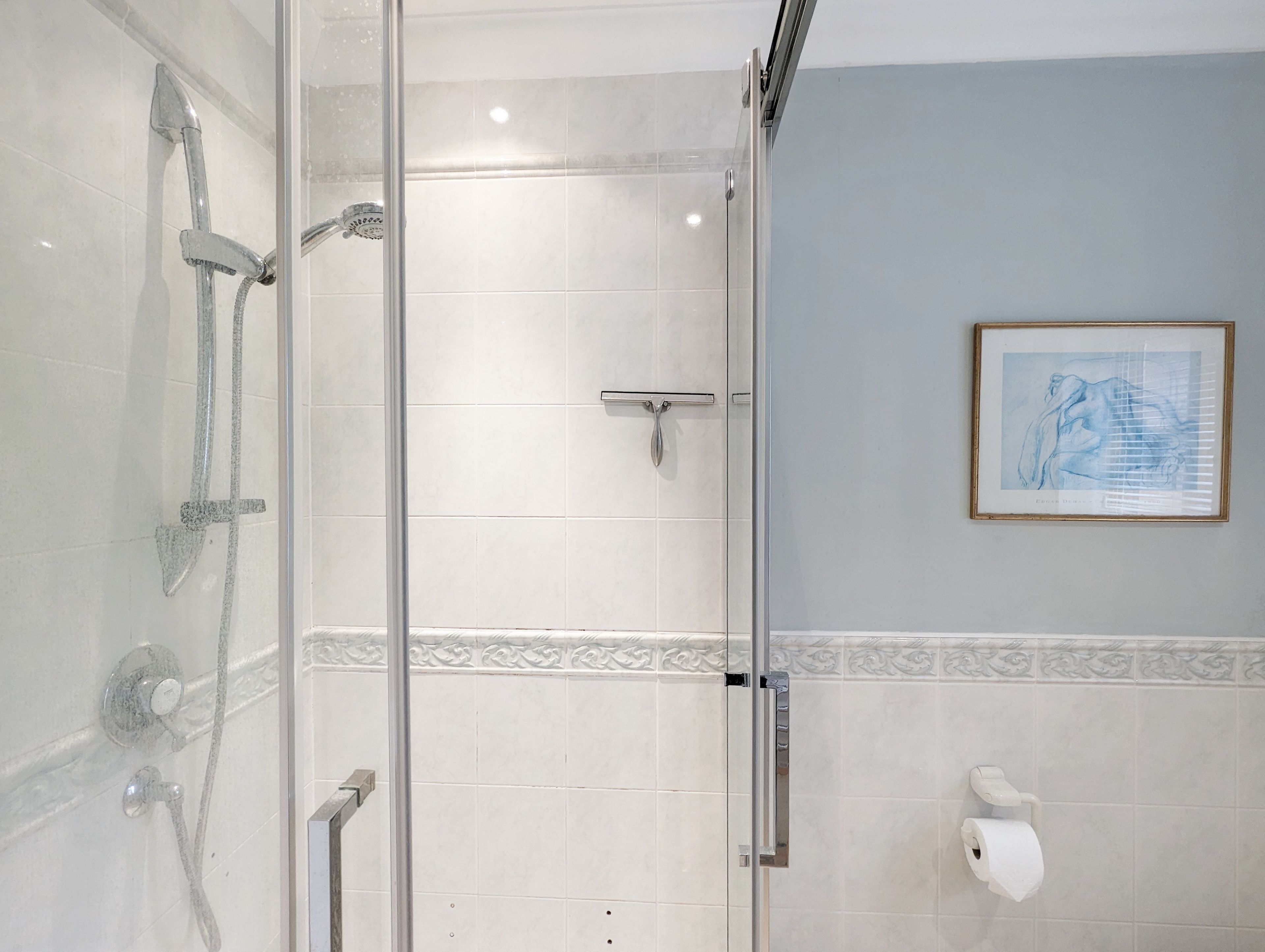 Een moderne badkamer met een douchecabine van glas, een handdroger en een gekaderd kunstwerk aan de muur.