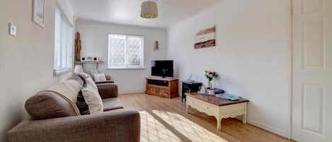 A living room with a sofa, TV, wooden cabinet, and a small table with a vase.