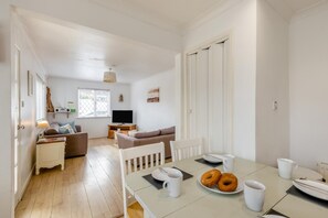 A modern, well-lit living area with a dining table set for breakfast, a sofa, and a television.