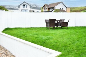 A well-maintained grassy backyard with a white wall, a concrete pathway, and a dining table with chairs.