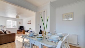 A dining area with a table set for four, a bottle of wine, and a vase with flowers.