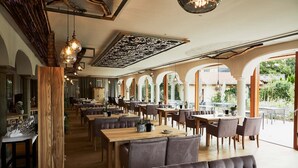 Um restaurante espaçoso com mesas e cadeiras de madeira, janelas amplas e um teto alto com vigas aparentes.
