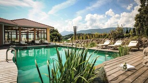 Uma área de piscina com espreguiçadeiras, um deck de madeira e um edifício com grandes janelas.