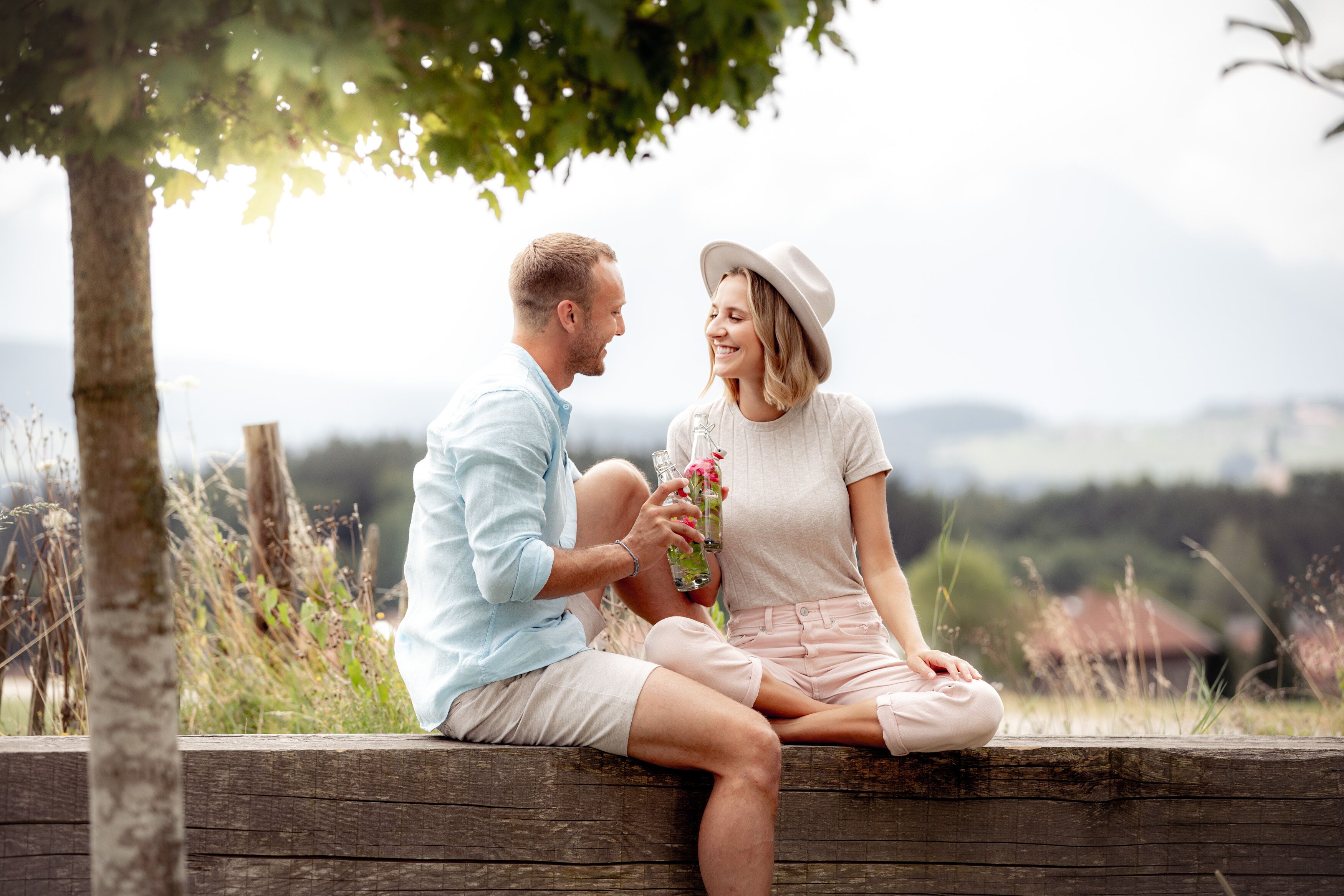 A couple sitting on a wooden bench outdoors, with a scenic view in the background.