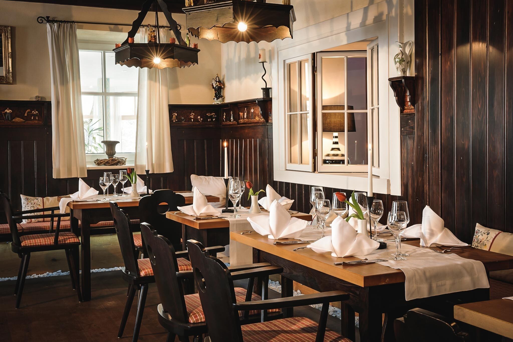 A dining area with wooden tables and chairs, white tablecloths, and candles.
