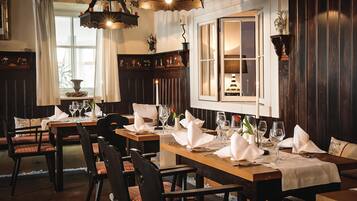 A dining area with wooden tables and chairs, white tablecloths, and candles.