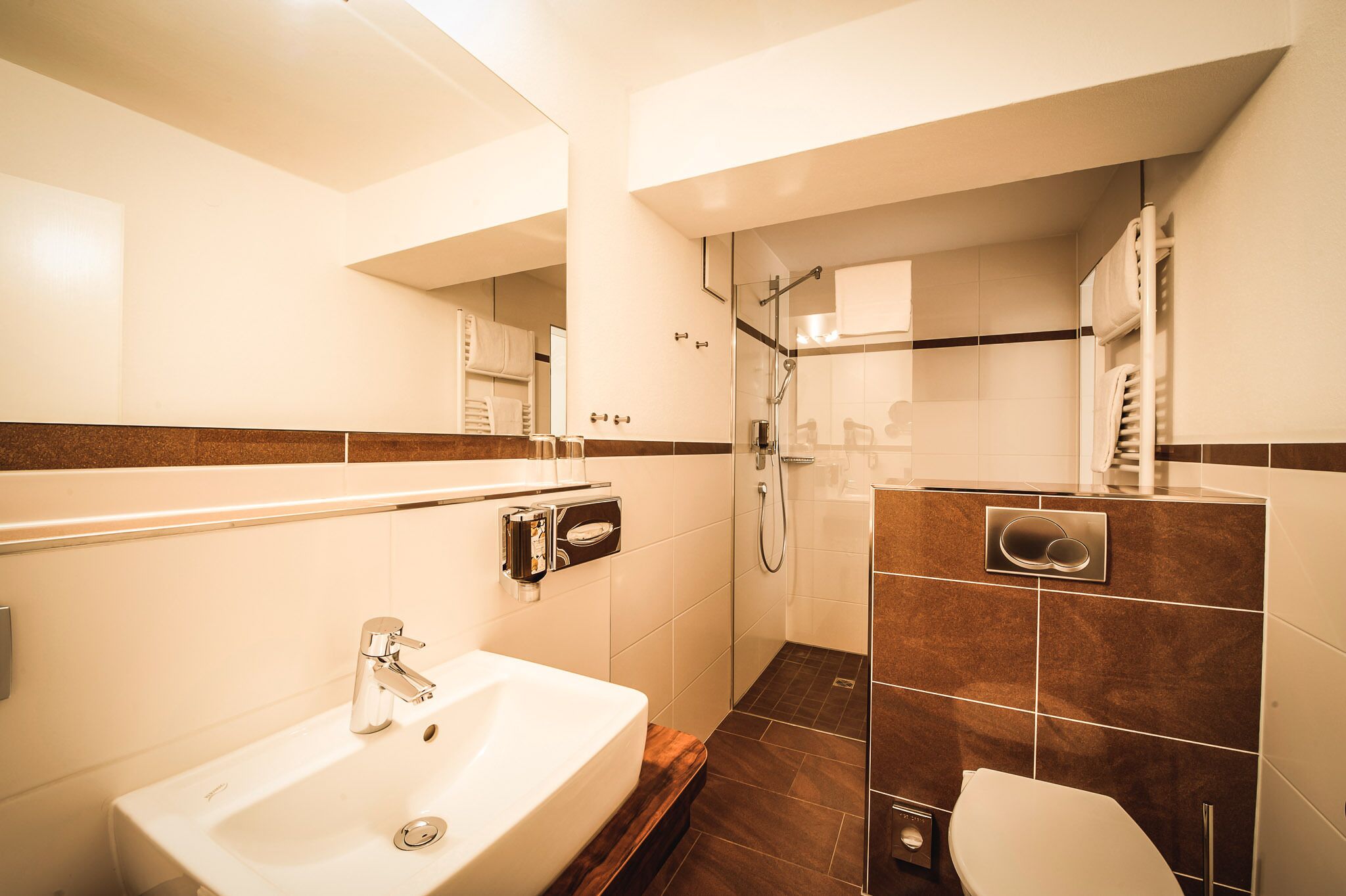 A modern bathroom with a sink, mirror, shower, and toilet.