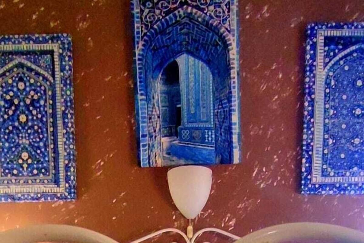 Un lit avec une tête de lit en métal, un mur orné d’œuvres d’art aux motifs bleus et un coussin à motifs rouges.
