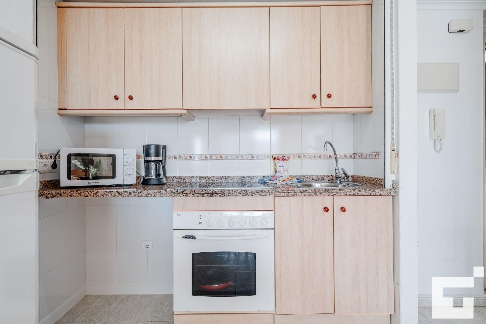 Une cuisine compacte avec des meubles de couleur bois clair, un plan de travail en granit, une machine à café, un grille-pain et un four encastré.
