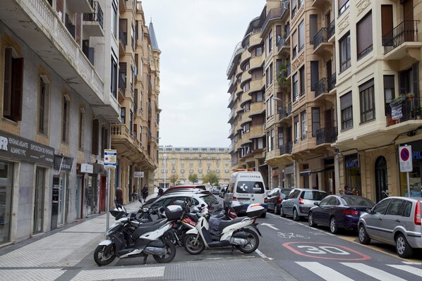 Una calle bordeada de edificios de varios pisos, coches aparcados y motocicletas.