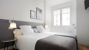 A modern hotel room with a large bed, two bedside tables, a small round table, and a window with a view of the city. - Miramon by FeelFree Rentals (San Sebastián)