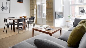 A modern living room with a stone wall, a dining area with wooden furniture, and a large window providing natural light. - Miramon by FeelFree Rentals (San Sebastián)