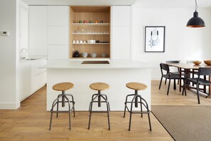 Una cocina moderna con armarios blancos, encimera de madera y tres taburetes.