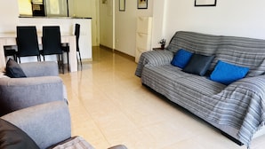 Een woonkamer met een bank, stoelen, een eettafel en een keuken op de achtergrond.