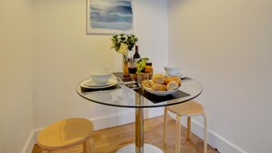 A small dining area with a glass table, two stools, a bowl of food, a bottle of wine, and a vase of flowers. - 1 Bed in Woolacombe (oc-seablu) (Woolacombe)