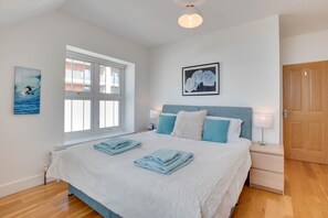 A bedroom with a large bed, a window, a framed picture, and a door.