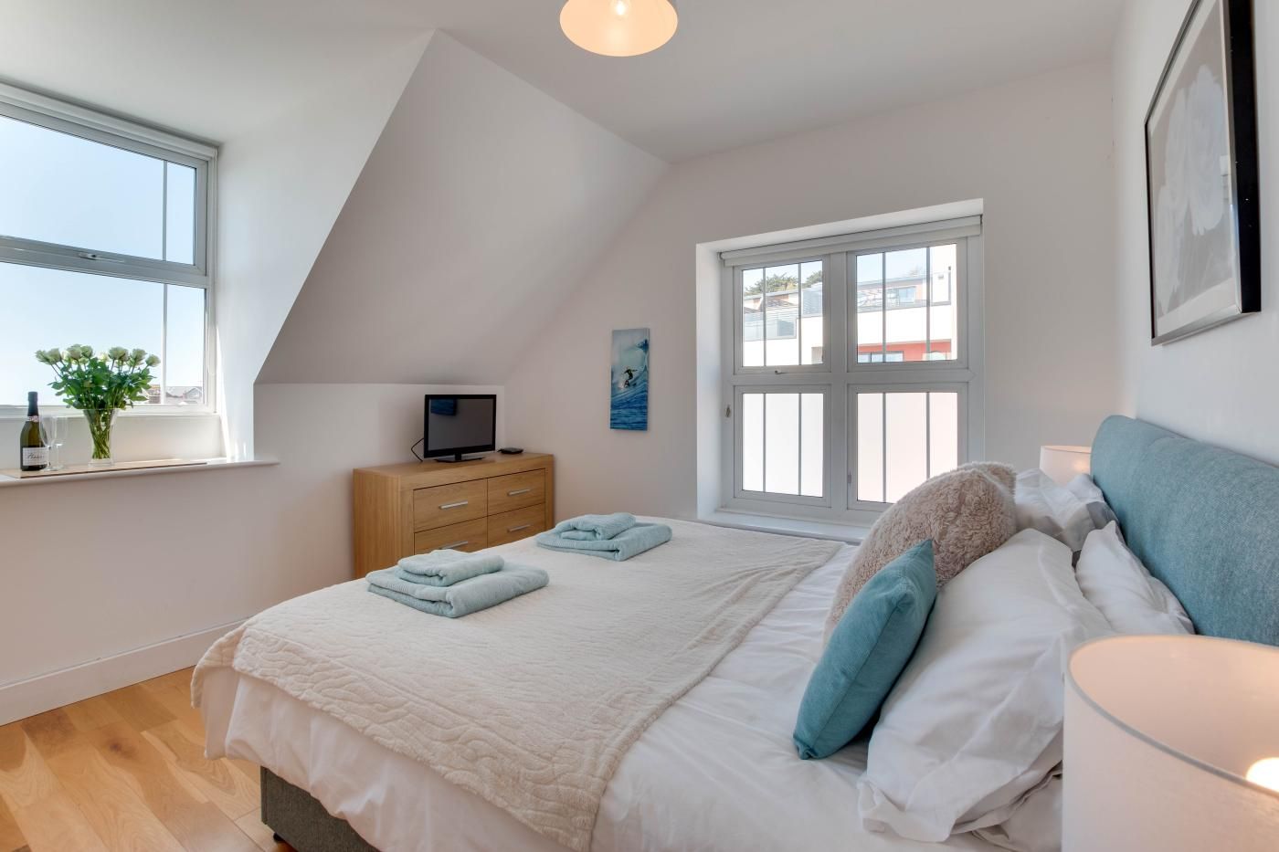 Ein Schlafzimmer mit Bett, einem Fernseher auf einer Holzkommode, einem Fenster mit Aussicht und einem Gemälde an der Wand.
