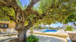 A pool area with a large tree, outdoor seating, and a view of the city skyline. - Villa Puchero - PlusHolidays (Calpe)