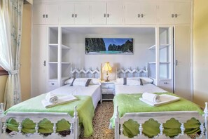 Quarto de hotel com duas camas, um quadro de uma praia e uma mesa de cabeceira com abajur.