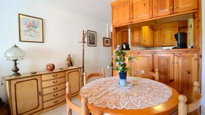 Un comedor acogedor con una mesa redonda de madera, mantel de encaje y sillas de madera. Se observa un aparador con cajones y una pequeña estatua sobre la mesa.