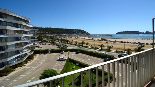 Vista costera con un estacionamiento, una playa y un edificio con varios balcones.