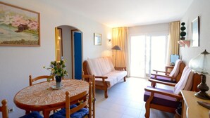 Una sala acogedora con una mesa redonda de madera, un sofá y dos sillones. Hay un cuadro en la pared y una ventana con cortinas.