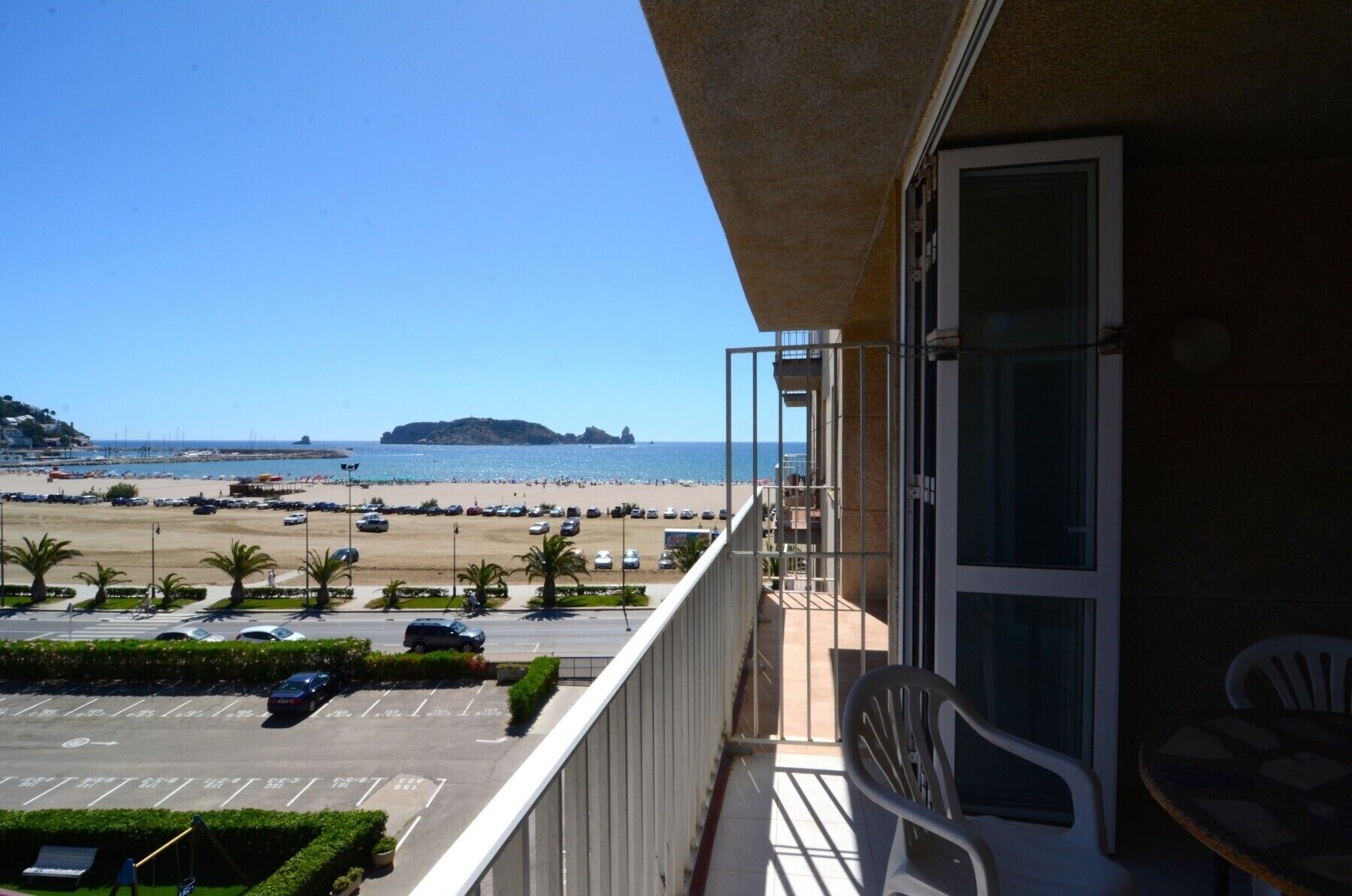 A balcony with a view of a beach, parking lot, and a distant island.