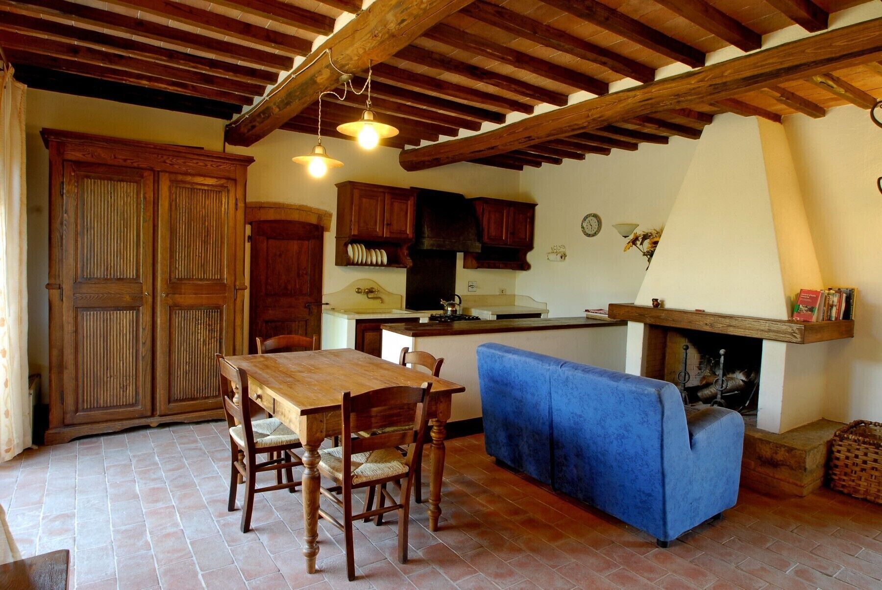 A rustic kitchen with wooden cabinets, a dining table with chairs, and a blue sofa.