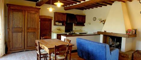 A rustic kitchen with wooden cabinets, a dining table with chairs, and a blue sofa.