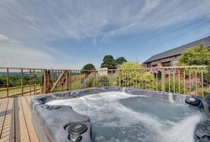 A hot tub with a wooden deck and a wooden fence, surrounded by a garden with various plants and flowers.