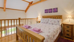 Une chambre avec un lit en bois, deux tables de chevet, une fenêtre et une structure de plafond en bois.