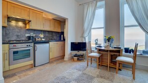 Une cuisine compacte dotée d’appareils électroménagers modernes, un coin repas avec une table et des chaises, et une grande fenêtre agrémentée de rideaux.