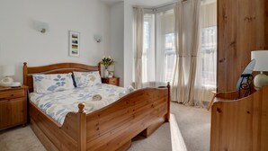 Un lit en bois dans une chambre avec une table de chevet, une lampe et une fenêtre ornée de rideaux légers.