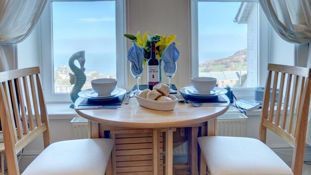 Un coin repas comprenant une table ronde, deux chaises, un vase avec des fleurs, une bouteille et un bol.