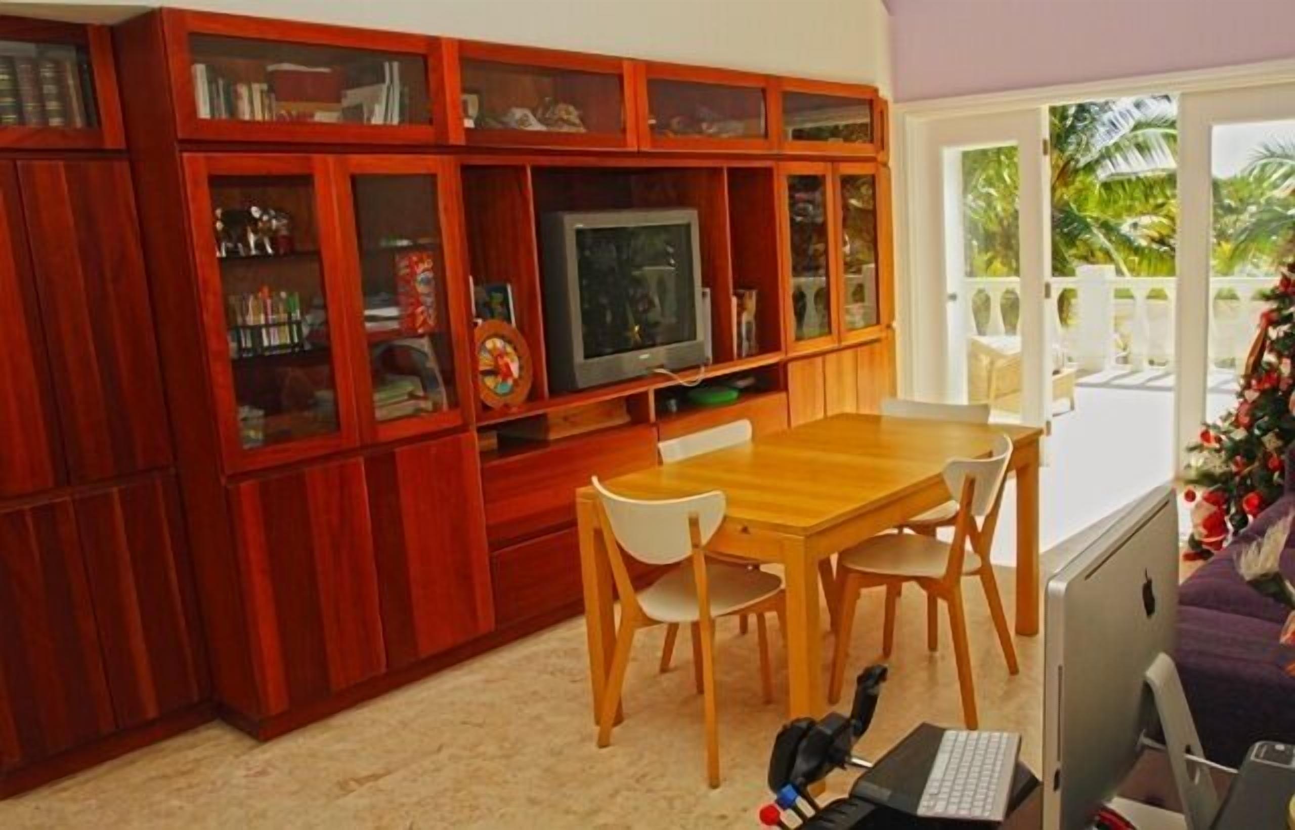 Una habitación con un mueble de televisión de madera, una mesa de comedor con sillas y un escritorio con una computadora portátil y teclado.