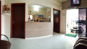 A reception area with a reception desk, chairs, a tiled floor, and a view of the outside through a glass door. - Hotel Premier (Campo Grande)