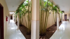 A corridor with white tiled floors, bamboo plants, and a fire extinguisher on the wall. - Hotel Premier (Campo Grande)