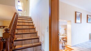 A staircase with wooden railings and beige steps leading to a room with a white wall, a sofa, and two framed pictures.