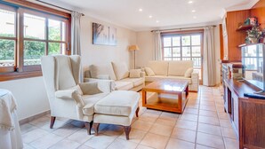 A spacious living room with a large window, a sofa set, a coffee table, and a TV on a wooden cabinet.
