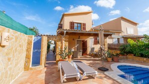 A Mediterranean-style villa with a swimming pool, outdoor seating, and a stone wall.