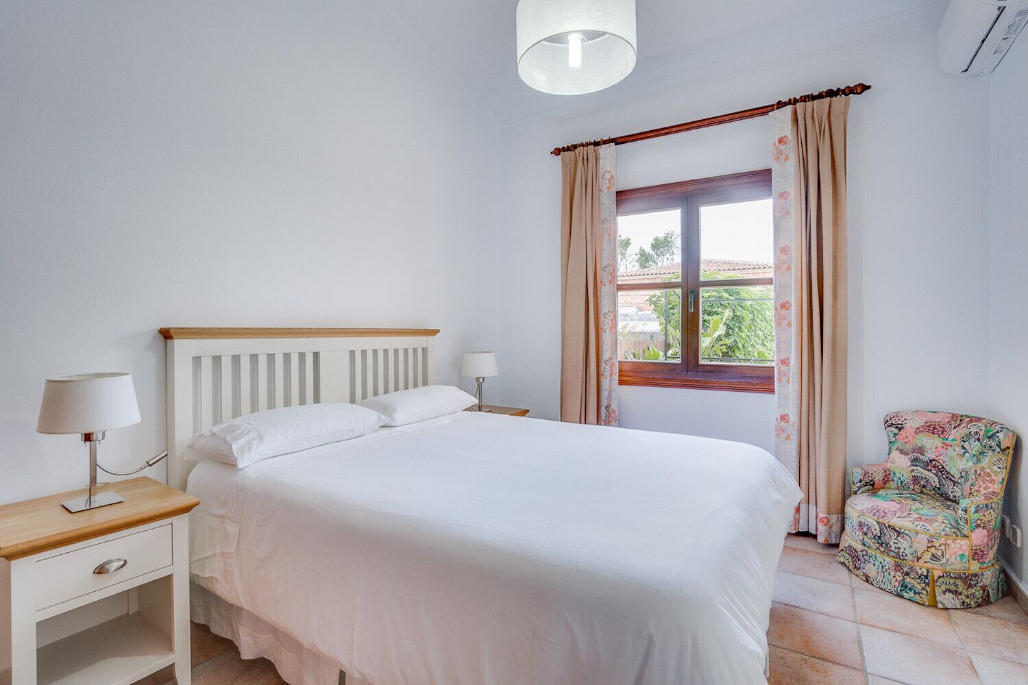 A bedroom with a bed, bedside tables, a chair, and a window with curtains.