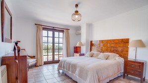 A bedroom with a large bed, a wooden headboard, a nightstand, a dresser, and a window with curtains.