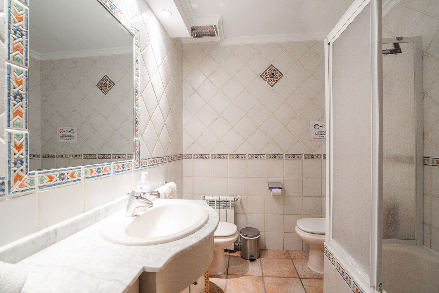 A bathroom with a sink, two toilets, a shower, and decorative tiles.