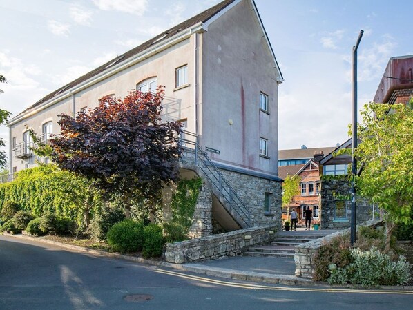 A building with a stone staircase leading to a flat entrance, surrounded by greenery and a clear sky.