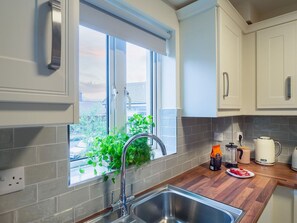 A kitchen with a window, a sink, cabinets, and a countertop with a kettle and coffee maker.